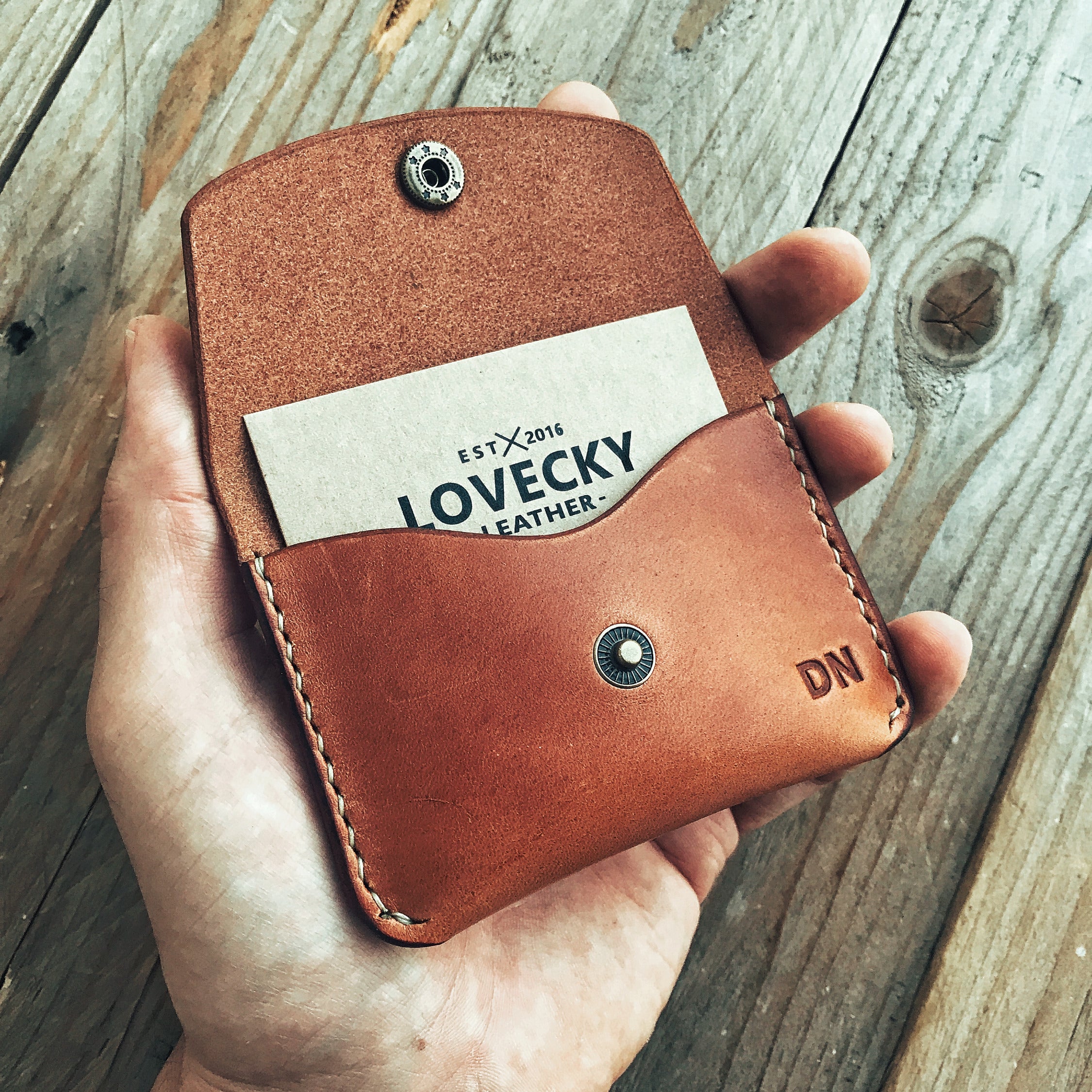 Lovecky Leather malá kožená peněženka 52 ve světle hnědé barvě, držená v ruce, ruční výroba z pravé kůže s gravírovaným monogramem, vhodná na karty a mince.